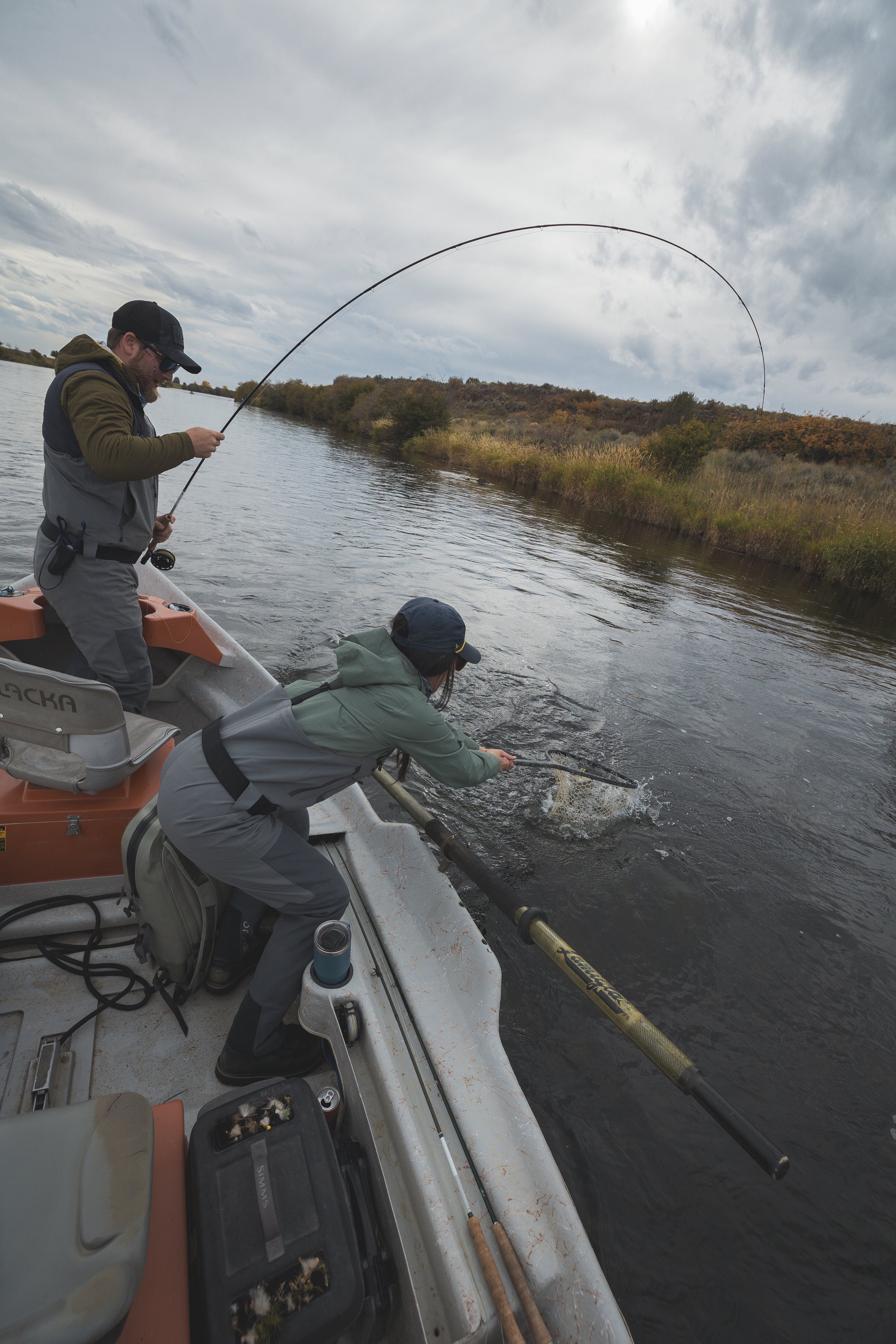 a guide netting a fish on the river with a fisherman holding a fly rod 