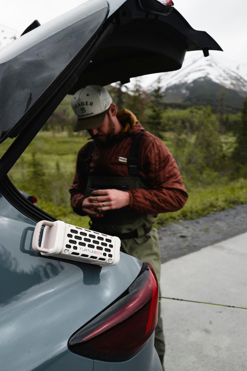 Turtle Box Ranger portable speaker by Turtlebox Audio on car trunk with fisherman and mountain scenery backdrop