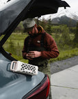 Turtle Box Ranger portable speaker by Turtlebox Audio on car trunk with fisherman and mountain scenery backdrop